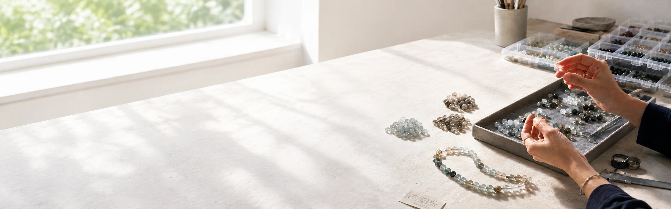 Hands sorting loose natural stone beads in a tray on a studio worktable